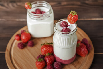 Strawberry raspberry yogurt in jar on wooden board close-up and copy space
