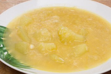 A close-up of a homemade porrusalda cod stew consisting of cod, potatoes, and leeks, placed on a rustic stone-like countertop on a white plate adorned with green floral elements.