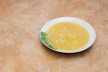 A white plate adorned with green floral elements, filled with homemade porrusalda cod stew consisting of cod, potatoes, and leeks placed on a rustic stone-like countertop. Traditional recipes.