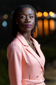 Portrait of a young woman at night with city lights reflecting in the water behind her