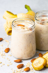 Almond banana smoothie with oat flakes in glass jars at white table.