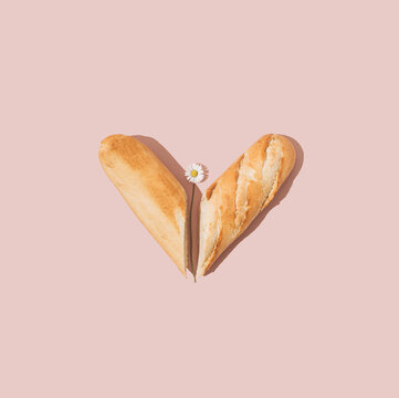 Heart made of fresh french baguette and daisy flower on pink background. Minimal summer food concept.
