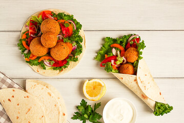 Tortillas, wrapped falafel balls, with fresh vegetables, vegetarian healthy food, on a wooden white background, no people, selective focus.