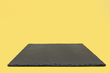 Black slate board on a yellow background. Empty space for text or design image. Slim slate coaster for cooking or restaurant menu. Free space for text