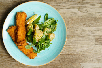 Fried cod fish fillet with potato salad, dijon mustard and a slice of lemon on a plate
