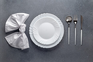 Place setting with white napkin, empty plate and silver cutlery on a gray concrete grunge table....