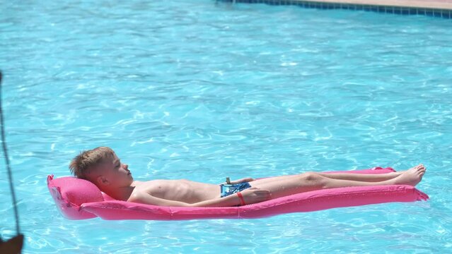 Happy child boy relaxing on inflatable air mattress in swimming pool on sunny summer day during tropical vacations. Summertime activities concept