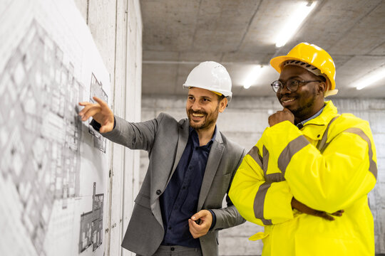 Construction worker in safety work wear and architect analyzing blueprint plan at the site.