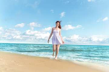 Fototapeta na wymiar Happy woman is walking along the sea coast. Smiling girl in a white dress on a background of blue sky and water