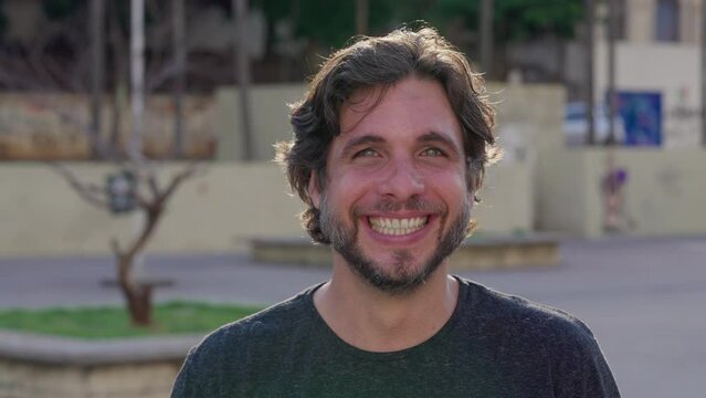 Portrait of a young man smiling at camera standing outside in city. One male person close-up face feeling happy