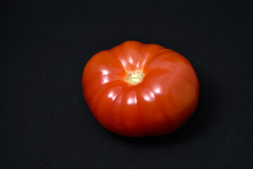 A large red tomato on a black background. Vegetables close-up.