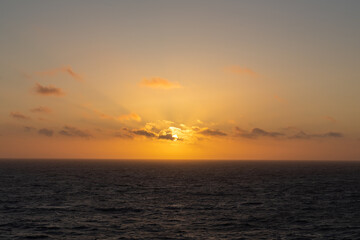 An orange sunset over the sea with light clouds.