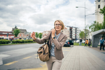 Fototapeta premium mature woman stand at city bus stop use smartphone while wait drive