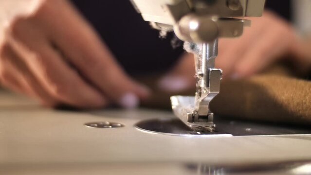 The process of creating from fabric in an electric sewing machine and sews the stitch along the edge into the bending. Female hands sewing on professional sewing machine.