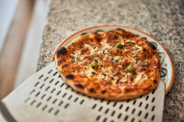 Male worker using a pizza shovel, putting a pizza on the plate.