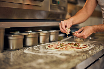 Male worker adding some mushrooms on top of pizza dough.