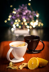 Black and white mug of linden tea and lemon in a tray on bokeh lighted background.