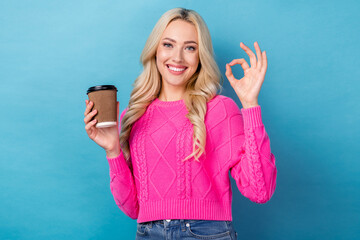 Fototapeta premium Photo of good mood pretty girl with wavy hairdo dressed pink sweater showing okey hold cup of latte isolated on blue color background