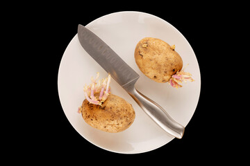 Two potatoes with sprouts with a metal knife on a white ceramic plate on a black background, macro,...