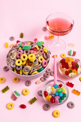 A bowl of cereal and candies with a pink spoon on a pink background