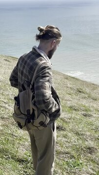 a white man with a beard and a backpack spends time along the ocean