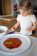 A little girl playing with plasticine and toys insects. Sensory development and experiences, themed activities with children, fine motor skills development