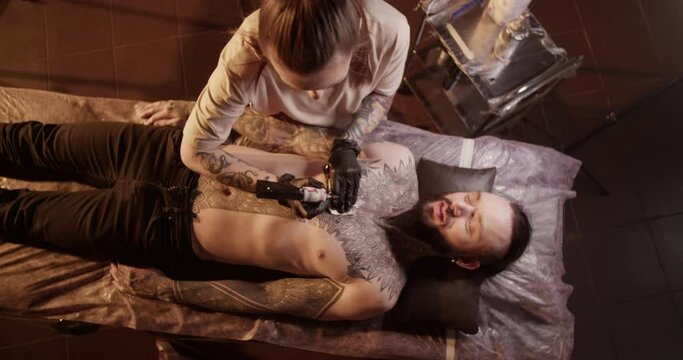 Female tattooist making tattoo on breast of smiling male customer