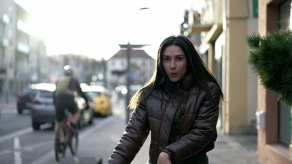 One carefree 20s woman dances outside in city street in celebration. Joyful female person dancing in urban sidewalk feeling happiness while walking toward camera closeup face