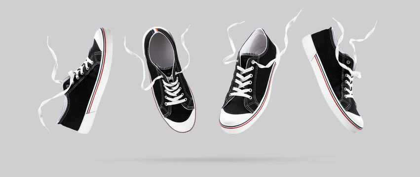 Flying black sneakers from different sides on gray background. Fashionable stylish sports casual shoes. Creative minimalistic layout with footwear. Creative template for design Mock up. Banner