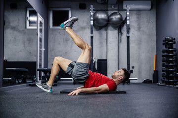 Buttocks and legs workout, muscle burning and functional strength training. A young man in sportswear rises to his heel as he raises his other leg in the air, leaning on his shoulders. Sport, gym