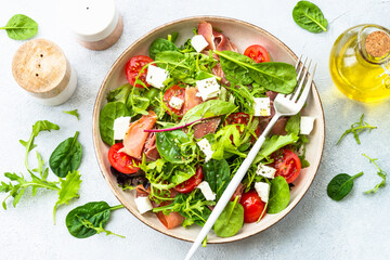 Healthy salad with green leaves, tomatoes and jamon. Top view in craft plate.