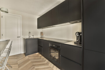 a kitchen with black cabinets and wood flooring on the walls, along with stainless stools in front of the counter
