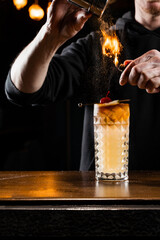 Burning cinnamon in cocktail. Bartender pours and fire burns cinnamon in alcoholic cocktail at a bar. Bartender is preparing alcoholic cocktail with whiskey, fresh lemon, sugar syrup and egg white.