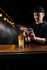 Bartender spraying and fire whiskey in alcoholic cocktail at bar. Bartender is preparing alcoholic cocktail with whiskey, fresh lemon, sugar syrup and egg white.
