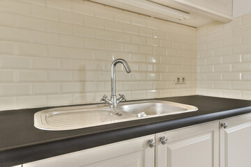 a kitchen with white tiles on the wall and black countertop in front of the sink is visible to the right