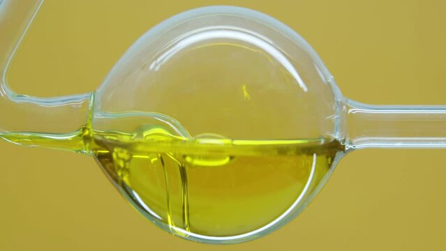 Yellow natural oil flows in a laboratory glass flask. Obtaining essential oils by filtration. Production of natural and organic cosmetics.  Skin care products. Absorb excess oil. Moisturizer. Mineral.