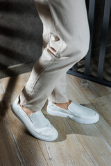 Fototapeta na wymiar Close-up of male feet in white casual shoes. Fashionable young man standing in leather stylish white moccasins in fashionable trousers. Seasonal summer men's shoes. Casual street style.