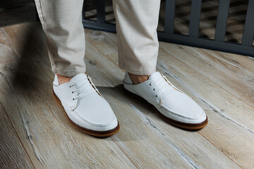 Fototapeta na wymiar Male feet close-up in white casual shoes. Fashionable young man standing in leather stylish white moccasins in trousers. Seasonal summer men's shoes. Casual street style.