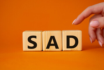 Sad symbol. Wooden cubes with words Sad. Businessman hand. Beautiful orange background. Business and Sad concept. Copy space.