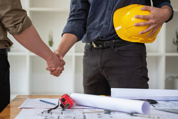 Asian engineers stand hand in hand to work together to document cost estimates and write floor plans for architectural and engineering designs for houses and buildings.