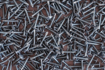 Chrome screws of silver color are scattered on the table.Sale of connecting screws made of stainless steel.Fasteners for metal.