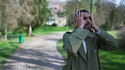 Troubled man covering face in shame and anxiety. A Desperate depressed Middle Eastern person stands outdoors at park feeling worry and preoccupation