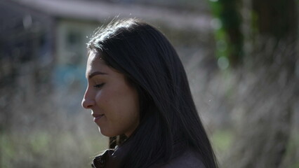 Profile face closeup of a contemplative young brunette woman walking outside at park feeling contentment and joy
