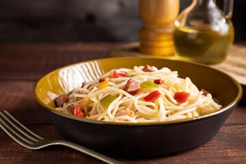 Plate with spaghetti, bacon and chopped vegetables.