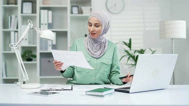 happy muslim arabic woman financier accountant calculates report and rejoices at good financial result Satisfied female entrepreneur or small business owner work with document PC Paperwork is pleasure