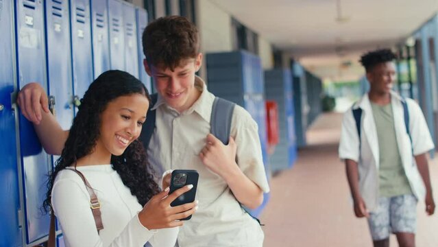 Two high school or secondary students looking at social media or internet on mobile phone by lockers - shot in slow motion