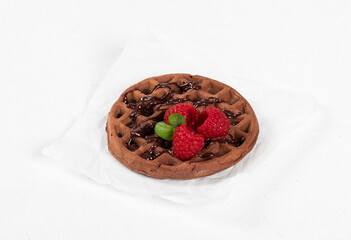 Cute Round soft chocolate waffle with raspberries. On paper. White background. Close up	