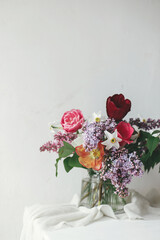 Stylish bouquet on rustic wooden table. Happy Mothers day. Spring lilac, tulips, daffodils arrangement on soft fabric in modern rustic room. Happy Womens day