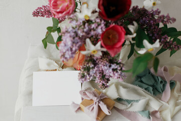 Happy Mothers day. Greeting card mock up and stylish bouquet with gift box and pastel ribbons on wooden table in modern rustic room. Space for text. Happy Womens day. Postcard mockup