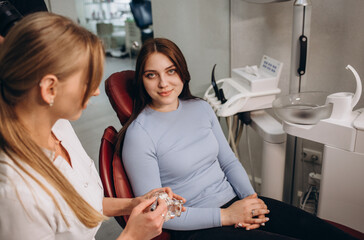 beautiful female dentist holds a model of the jaw and teeth in her hands on which she explains the structure to a girl patient. oral hygiene an example of a jaw in plastic. teeth layout.